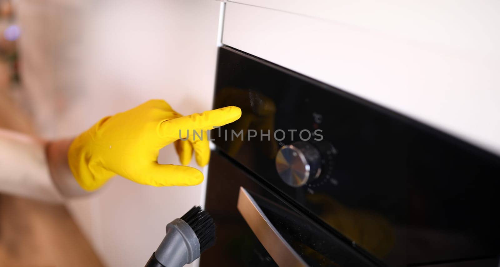 Housewife in yellow gloves cleaning stove brush. Cleaning tiles with steam cleaner. Hands in rubber gloves clean ceramic panel. Coronavirus steam cleaner disinfection. Shiny polished slab surface