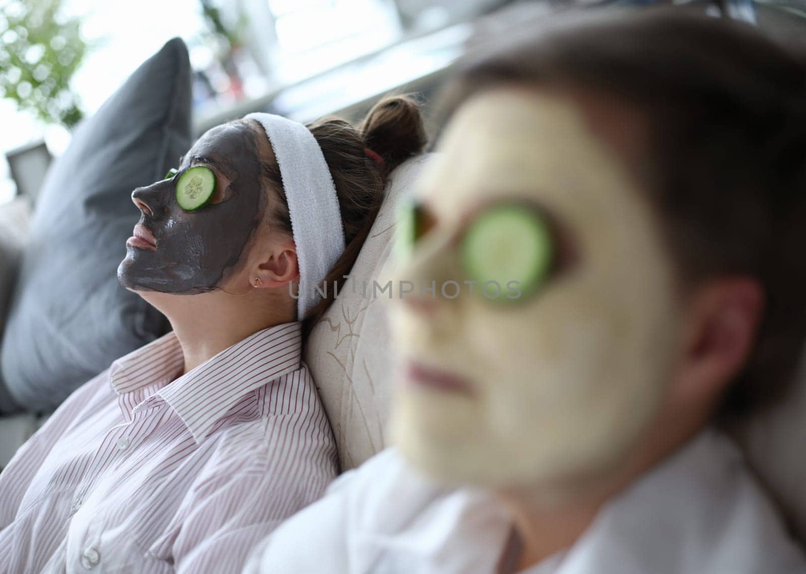 People are lying on couch with cosmetic mask faces. Man and woman lie with mask on faces cucumbers. Weekend relaxation. Matting masks for skin. Cucumbers on eyes to moisturize eyelids