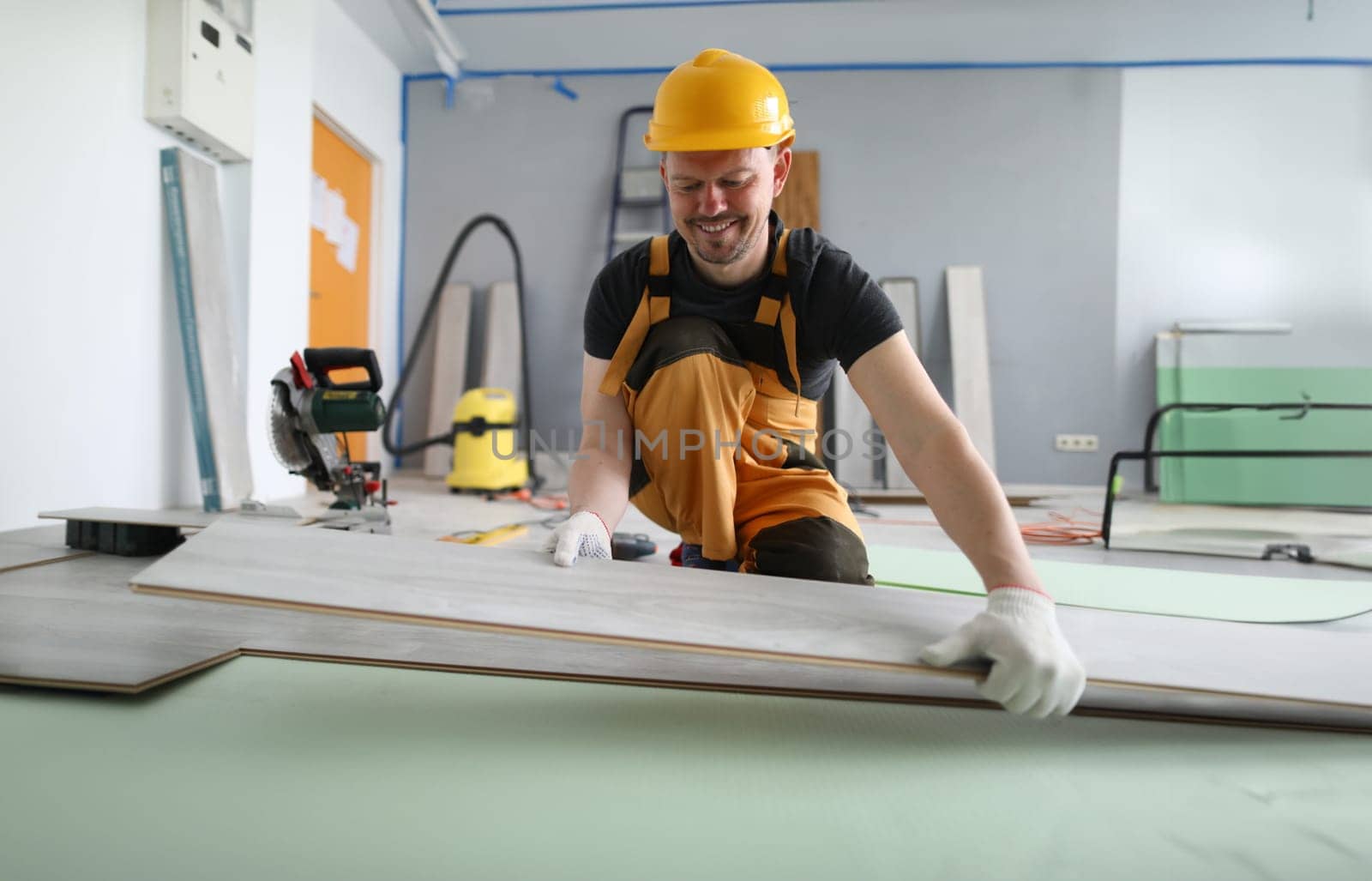Happy carpenter places laminate panels on floor. Man gives instructions for laying substrate and laminate. Simplicity in installation floor material. Serial connection one board with another