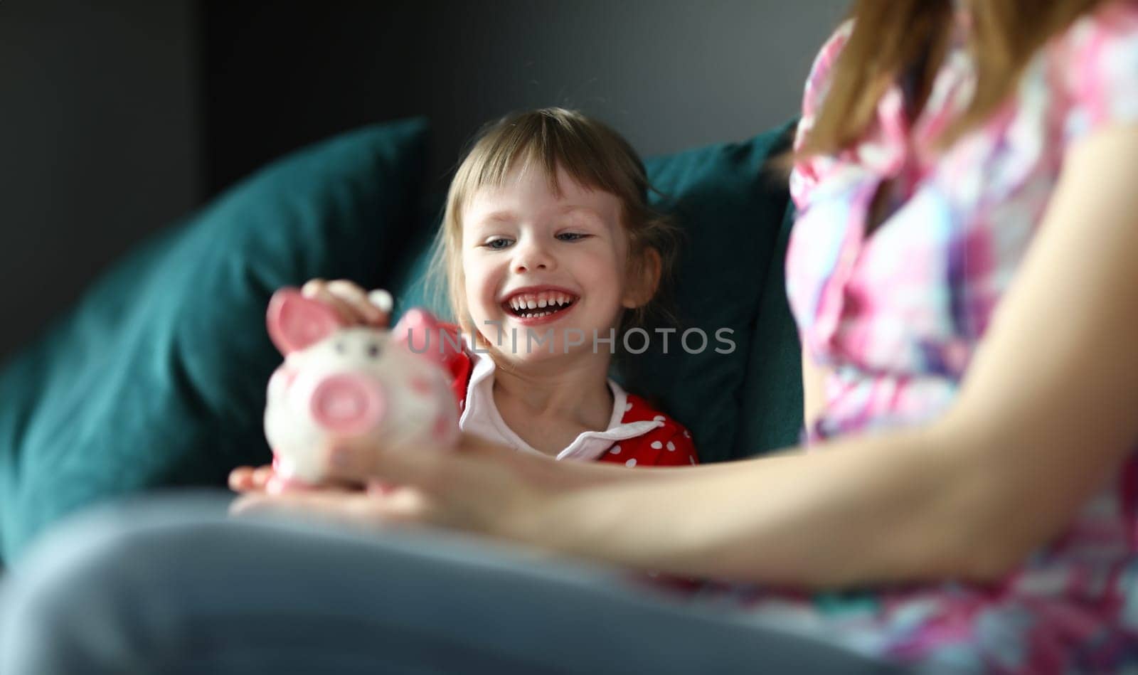 Little girl laughs and puts coin in piggy bank by kuprevich