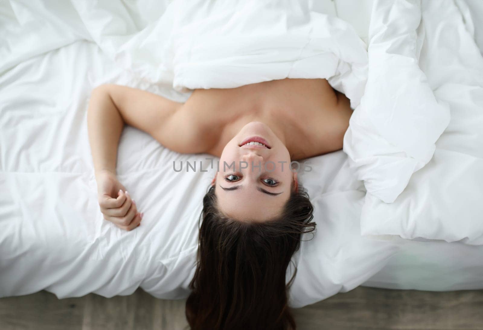 Smiling naked girl lies in comfortable soft bed. Girl woke up in good mood and smiling. Help defuse and release muscle clamps. Hypoallergenic bedding. Early awakening in apartment