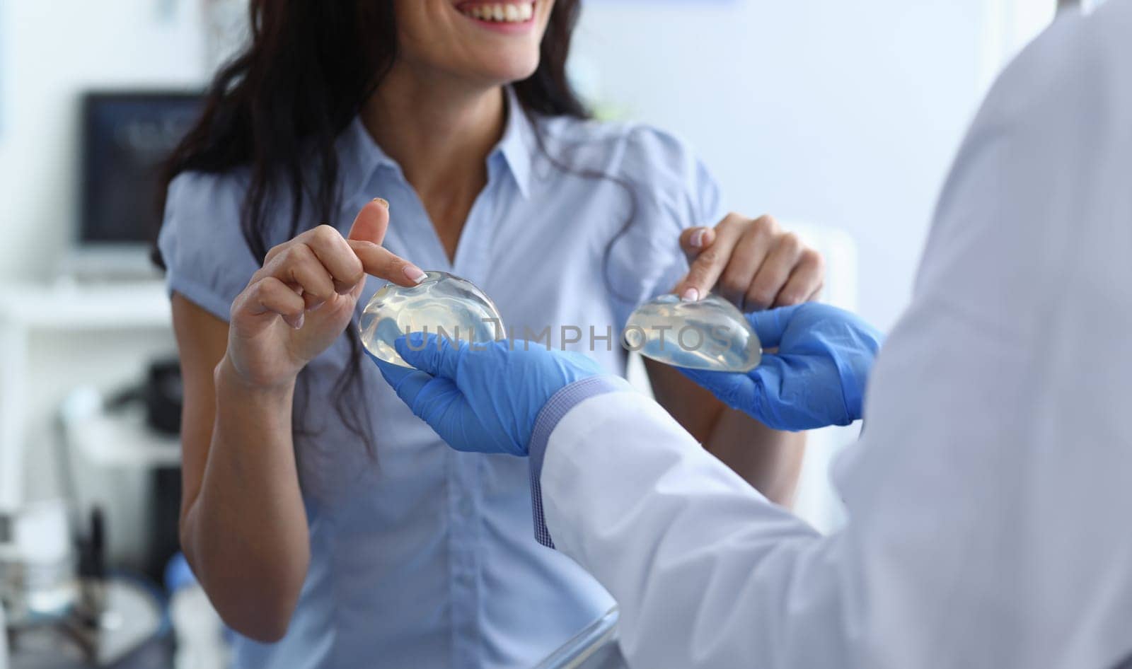 Laughing woman chooses breast implants from doctor. Doctor offers girl choice silicone breast implants. Medical consultation or recommendation plastic surgeon. Enlarge the breast and change its shape