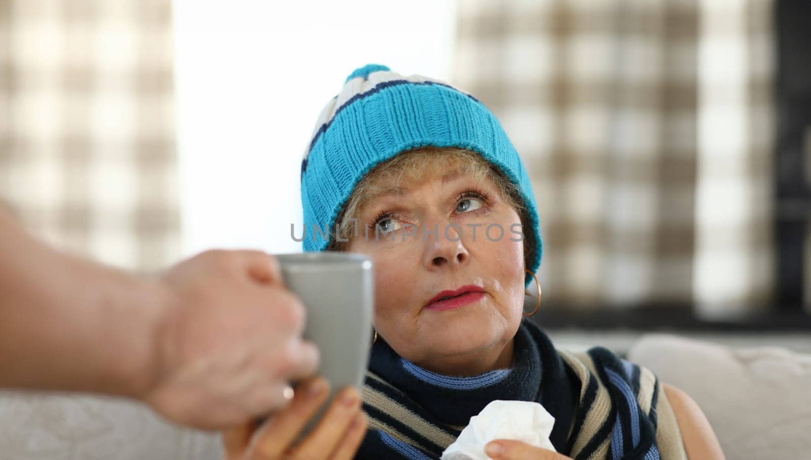 Sad elderly woman at home takes cup with hot drink. Son brought cup tea for an elderly mother. Son takes care an elderly mother at home. Good family relationships. Expresses warm feelings mother