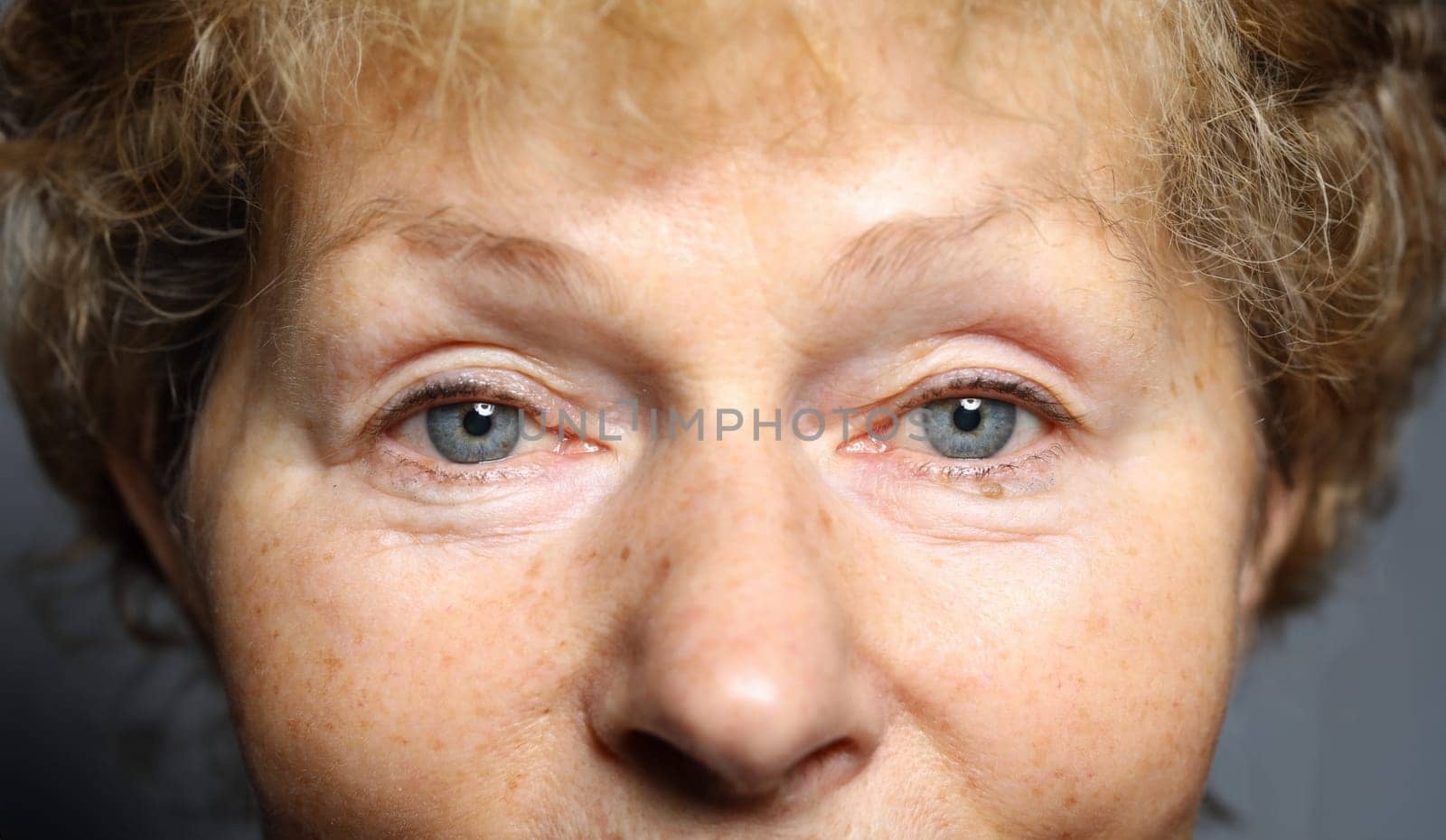 Tired look an elderly woman European appearance. Close-up, smiling face woman. Female face without makeup and intervention plastic surgeon. Correction defects. Microblading or hardware-based eyebrow