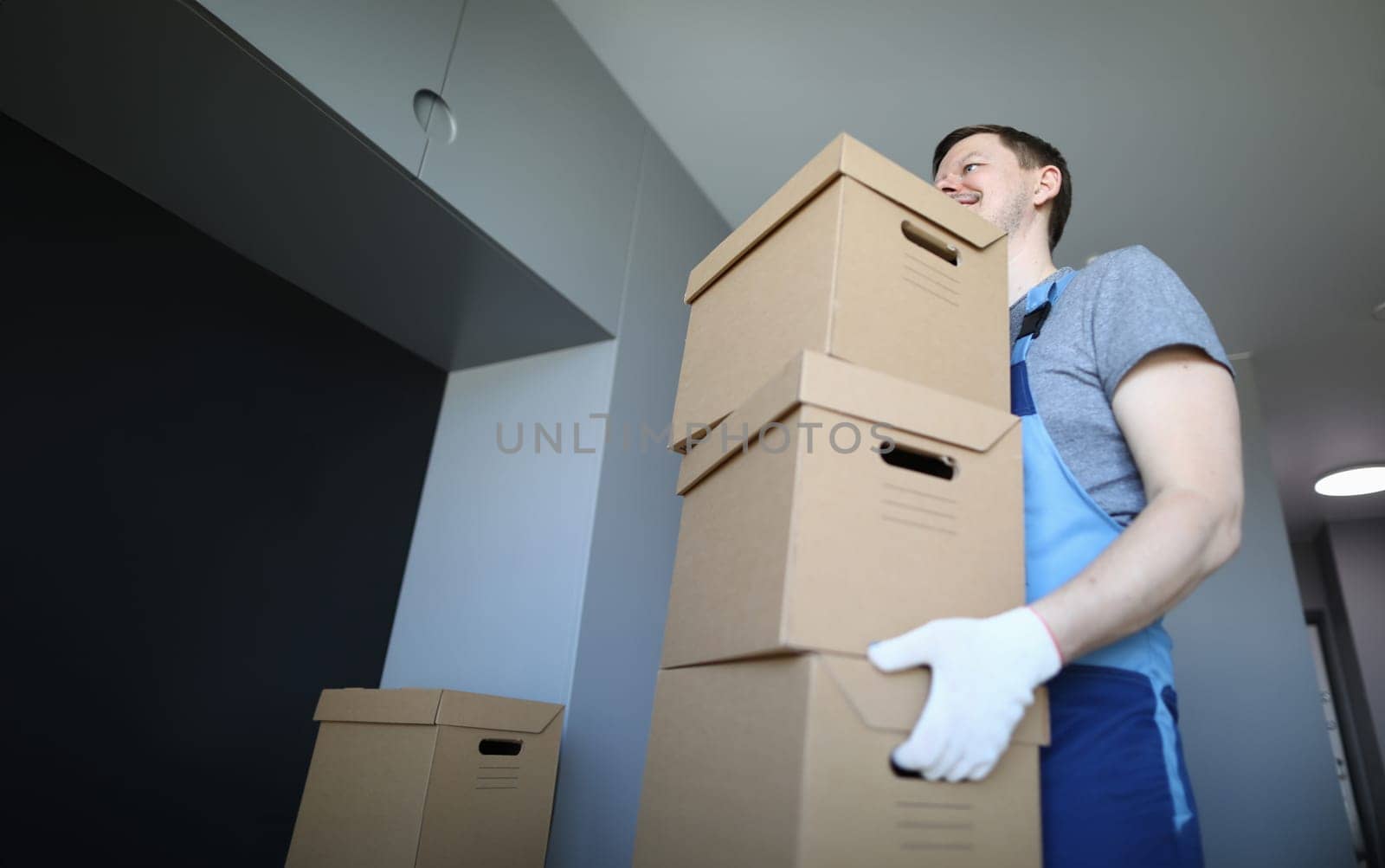 Male loader carries empty cardboard boxes indoors. Man in work clothes and gloves carries boxes. Folding drawers. Things are collected for moving. Collection goods in warehouse online store