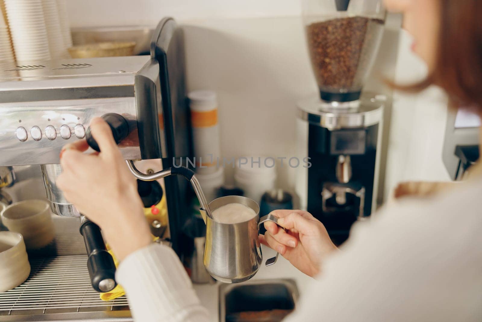 Close up of female barista frothing milk for coffee with professional coffeemaker working in cafe