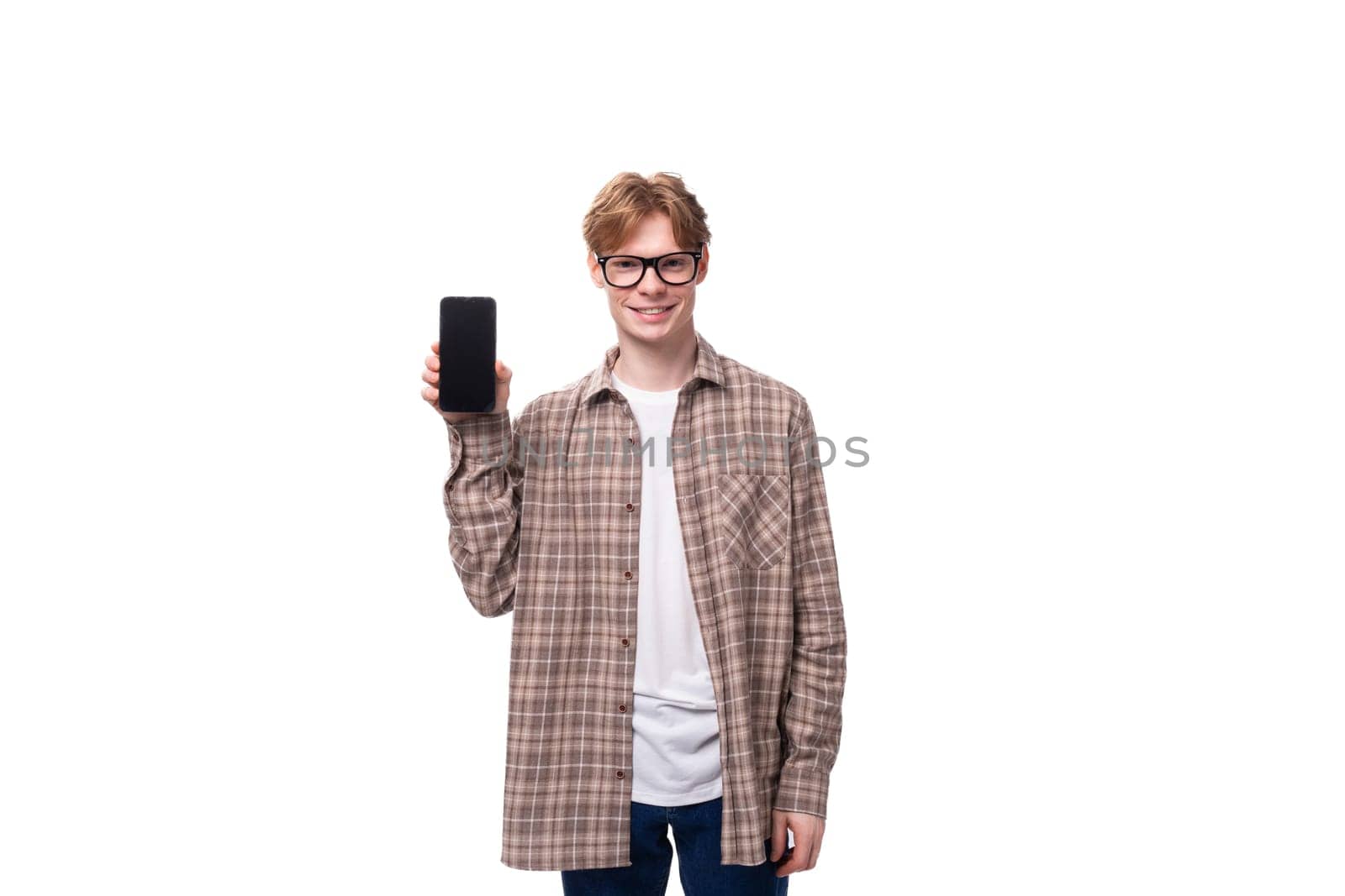 young stylish man with red hair dressed in a summer shirt shows the screen of a vertical smartphone with a mockup.