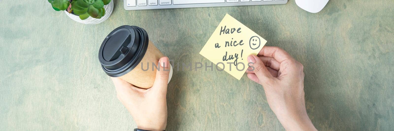 banner of female hands hold note with words HAVE A NICE DAY with smile and coffee in papper cup, keyboard, cactus and mause on a wooden table. concept of good start to day. top view of the desktop. Flat lay