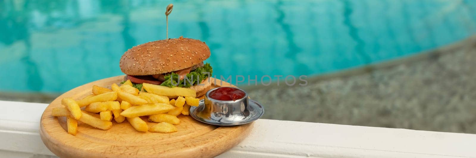 banner of tasty hamburger, appetizing french fries and ketchup. concept of relaxing and eating by the sea on a bright, hot and sunny day on the beach. soft focus by Leoschka
