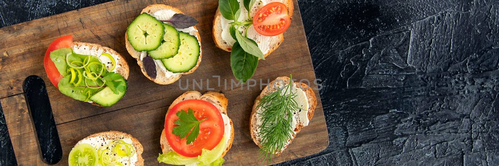 banner of six vegetable sandwiches with cream cheese, tomatoes, dill, cucumbers, leeks and basil. serving a vegetarian sandwiches for appetizers on cutting board. top view by Leoschka