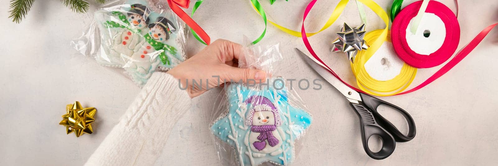 banner of female hands are packing Christmas gifts with gingerbread with snowmen on a gray background with scissors, colorful ribbons, bows. soft focus. by Leoschka