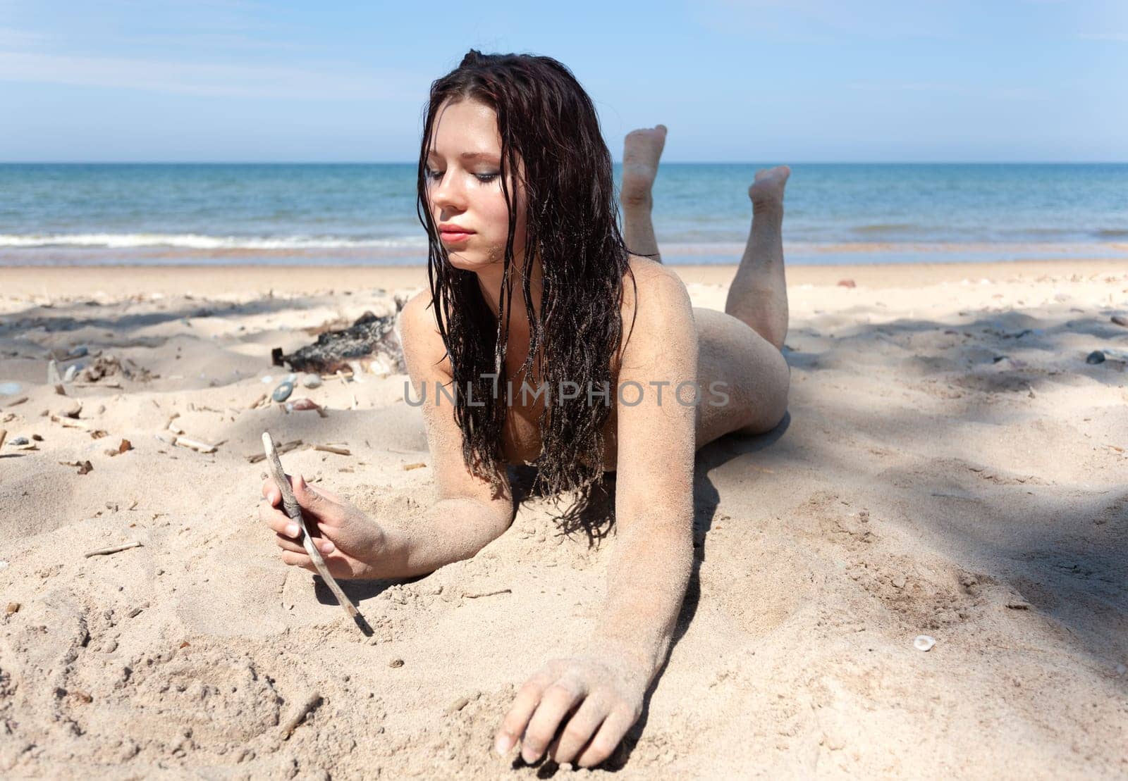 Nude woman with body covered by sand on sea coast by palinchak