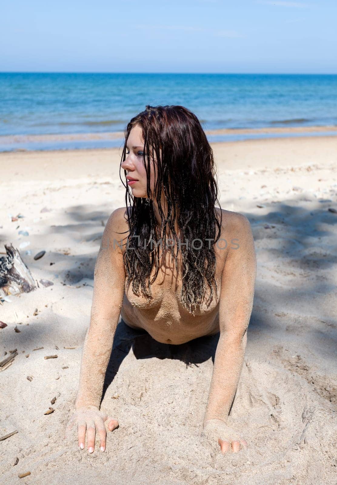 Nude woman with body covered by sand on sea coast by palinchak