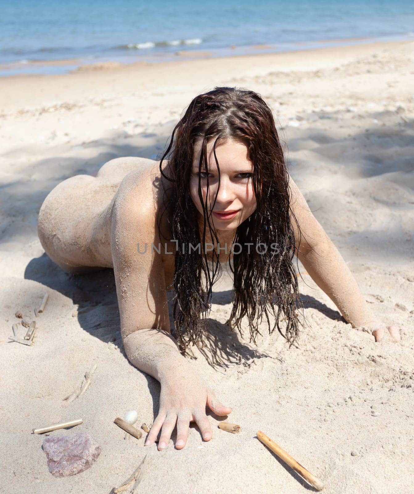 Youth, beauty, healthy lifestyle and nudity. Young fully naked woman with body covered with sand on the sea coast on a sunny day.