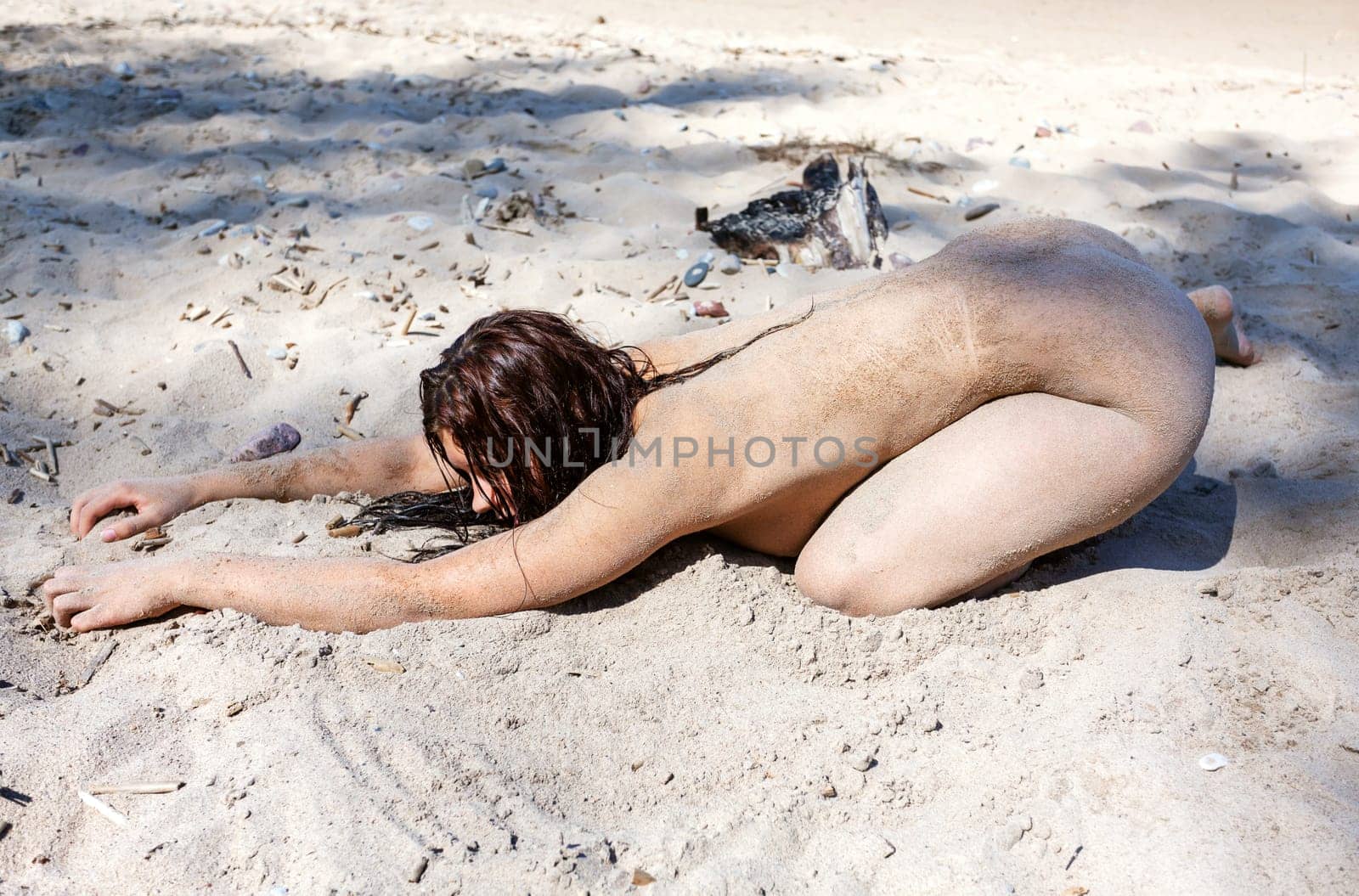 Youth, beauty, healthy lifestyle and nudity. Young fully naked woman with body covered with sand on the sea coast on a sunny day.