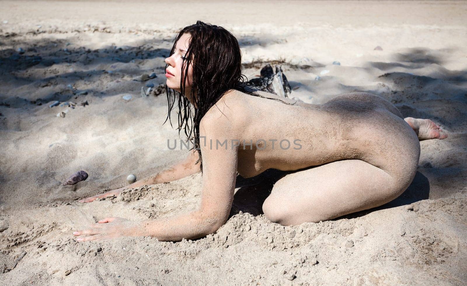 Youth, beauty, healthy lifestyle and nudity. Young fully naked woman with body covered with sand on the sea coast on a sunny day.