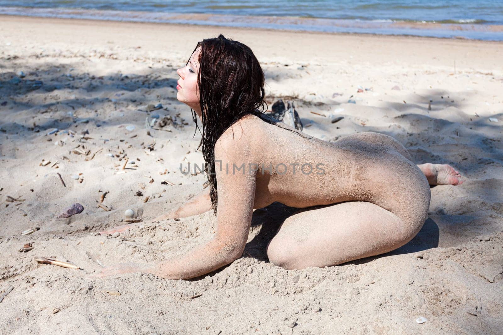 Nude woman with body covered by sand on sea coast by palinchak