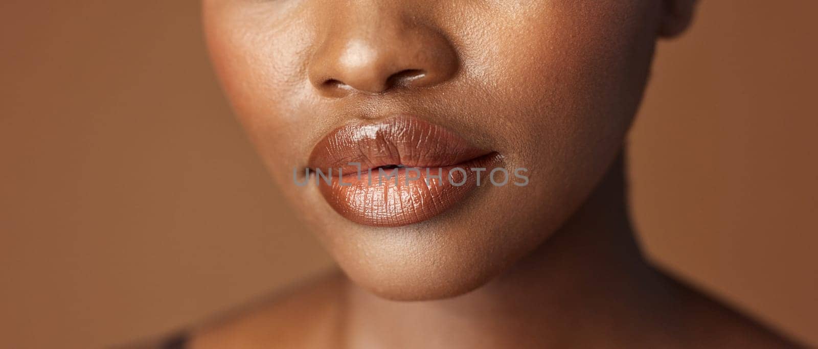 Closeup, lips and black woman with beauty, smile and skincare on a brown studio background. African person, girl and model with gloss, cosmetics and dermatology with clear skin, smooth and aesthetic by YuriArcurs