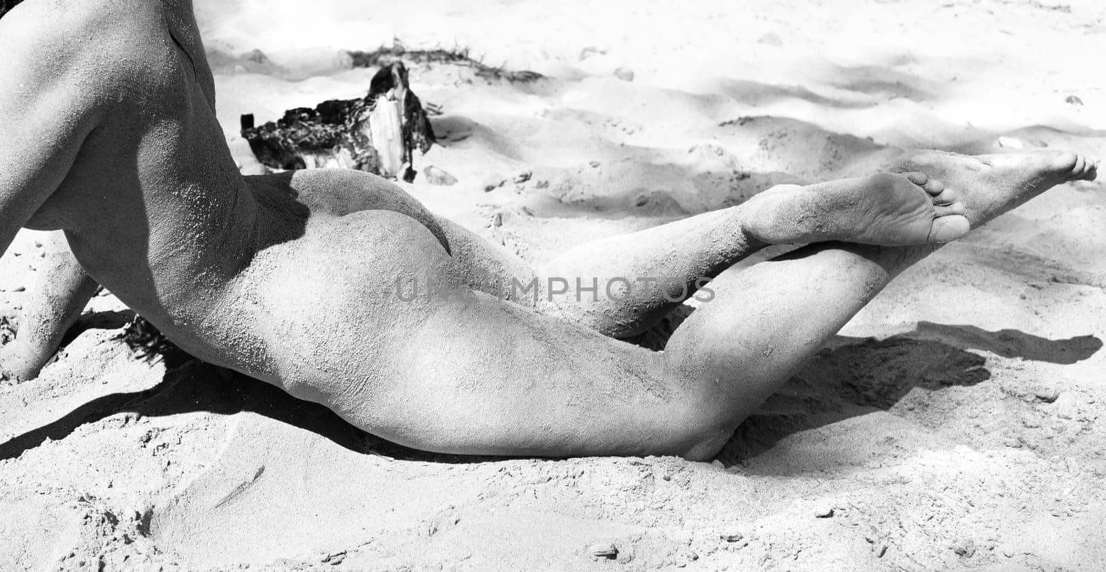 Youth, beauty, healthy lifestyle and nudity. Young fully naked woman with body covered with sand on the sea coast on a sunny day.