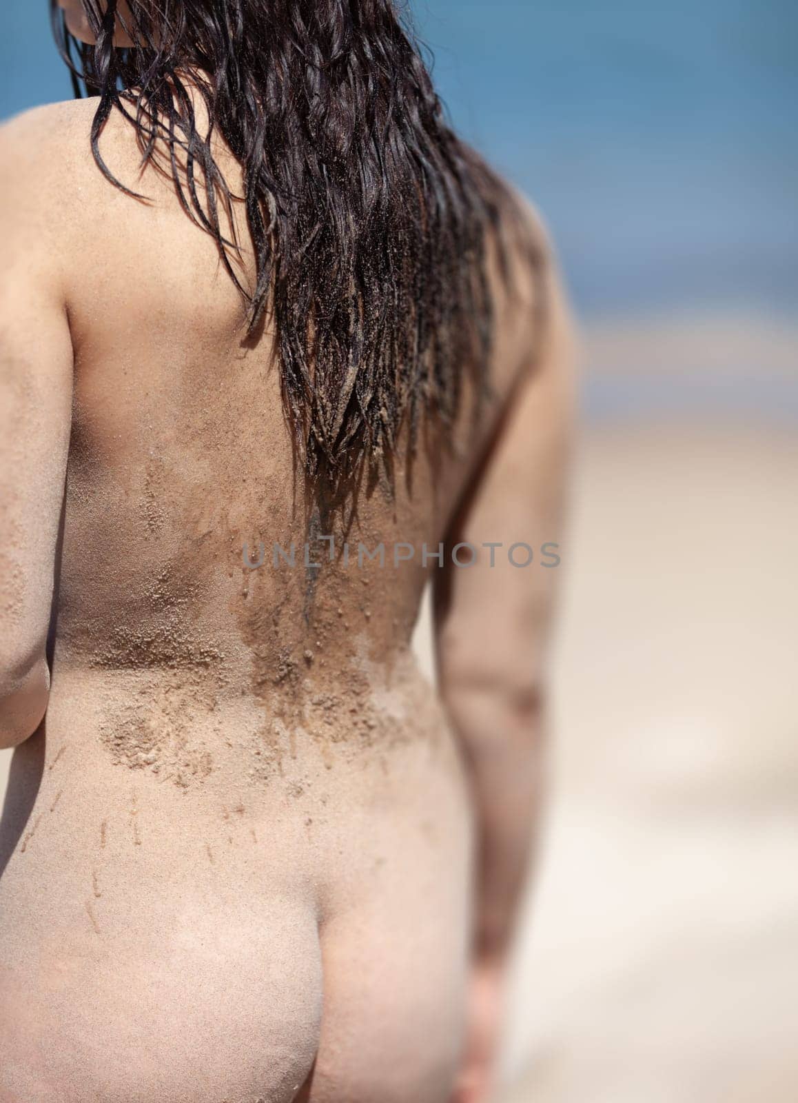 Youth, beauty, healthy lifestyle and nudity. Young fully naked woman with body covered with sand on the sea coast on a sunny day.