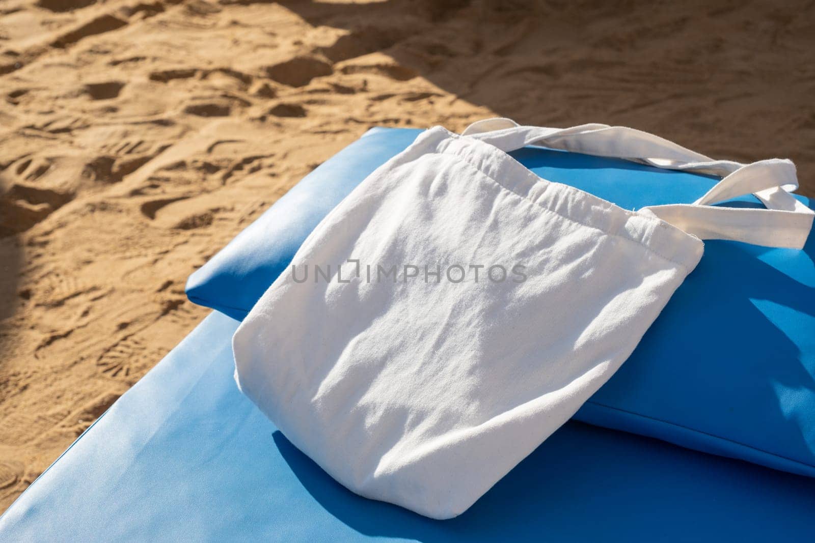 Mockup shopper handbag on blue lounger, beach sand background. Top view copy space shopping eco reusable bag.