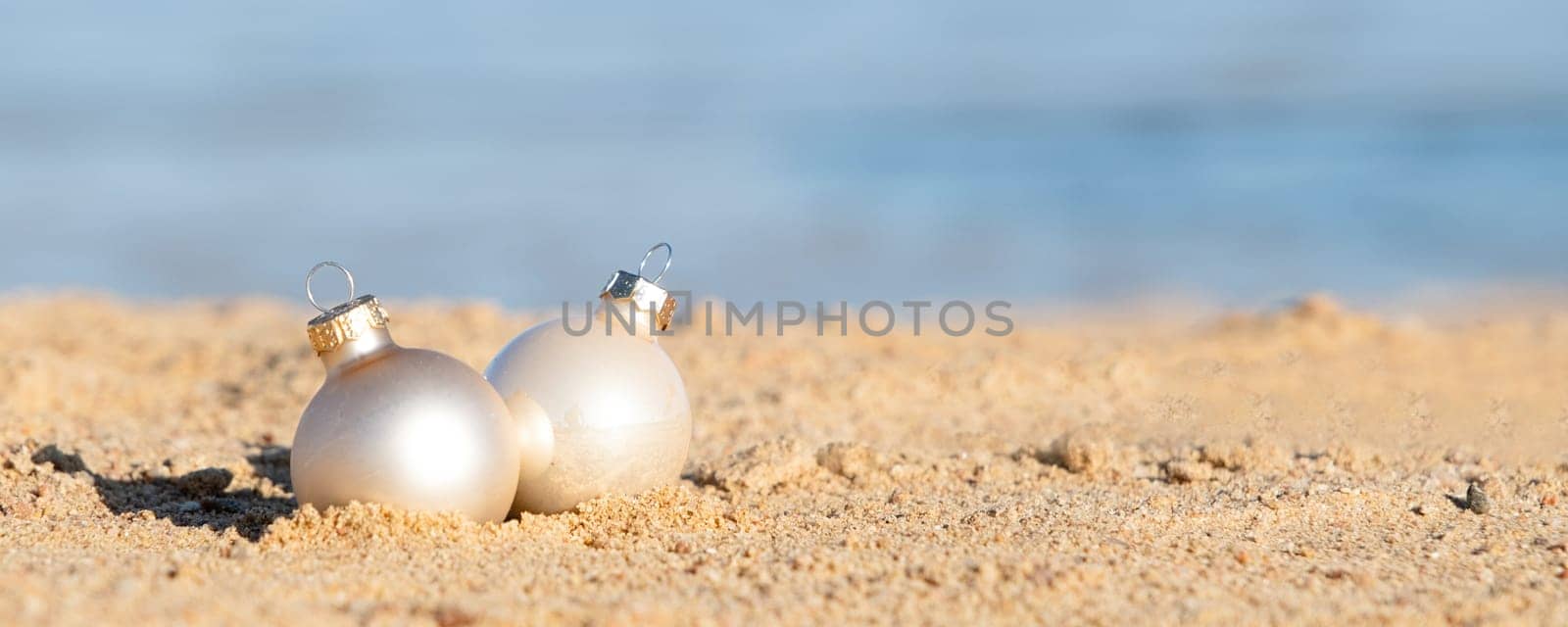 celebrating Christmas in hot countries. Christmas decorations bauble ball on sandy beach with sea background. copy space