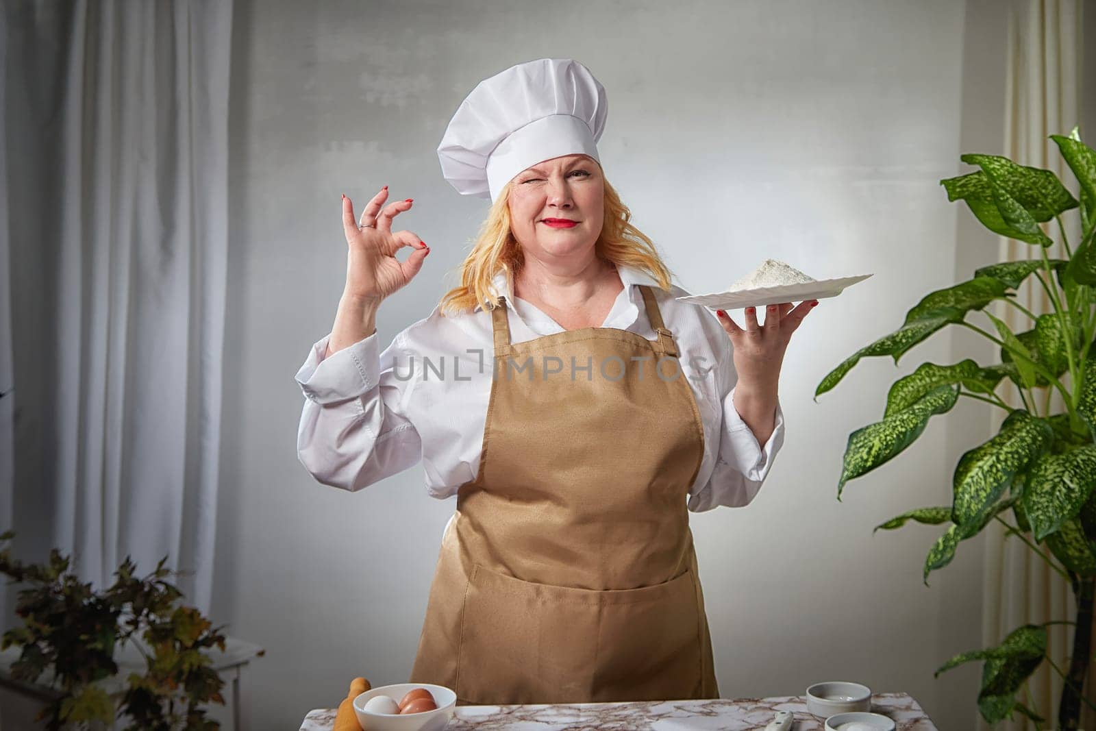 A fat funny female cook in a hat and apron poses in the kitchen and takes selfie. Good cooking and body positive