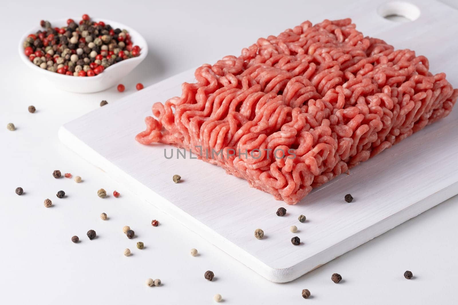 Fresh raw minced meat and peppers on a white table, close-up.