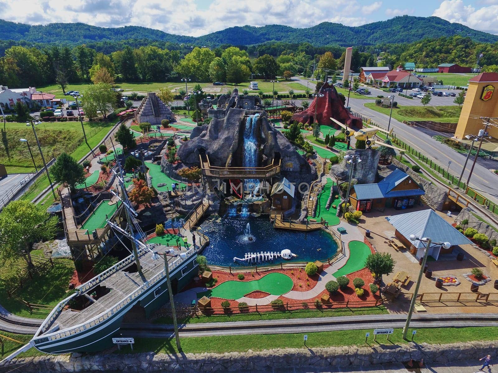 Aerial view of a bustling, colorful miniature golf course in tourist-friendly Gatlinburg, Tennessee, highlighting a pirate ship, waterfalls, and a volcano.