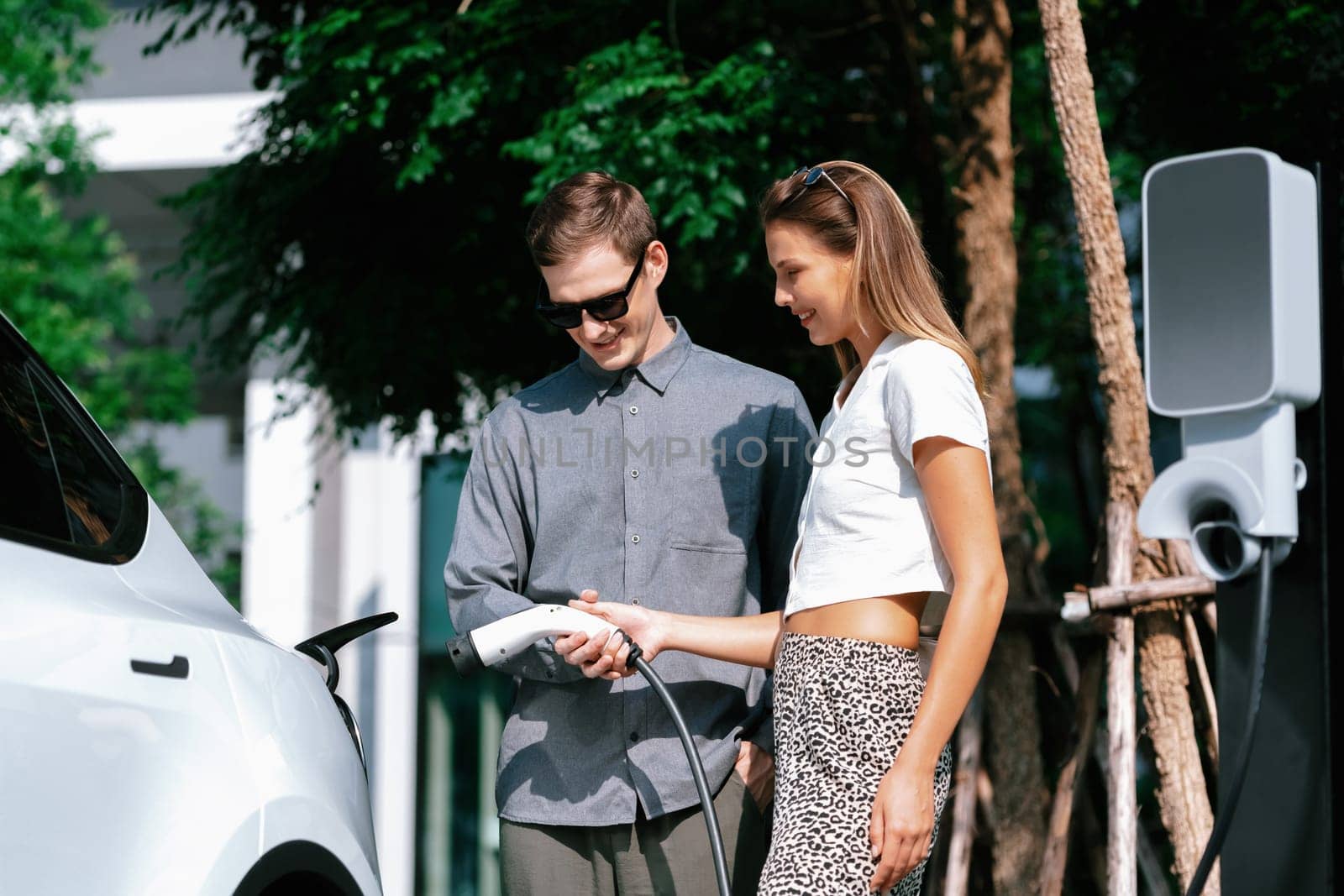 Young couple travel with EV electric car in green sustainable city innards by biancoblue