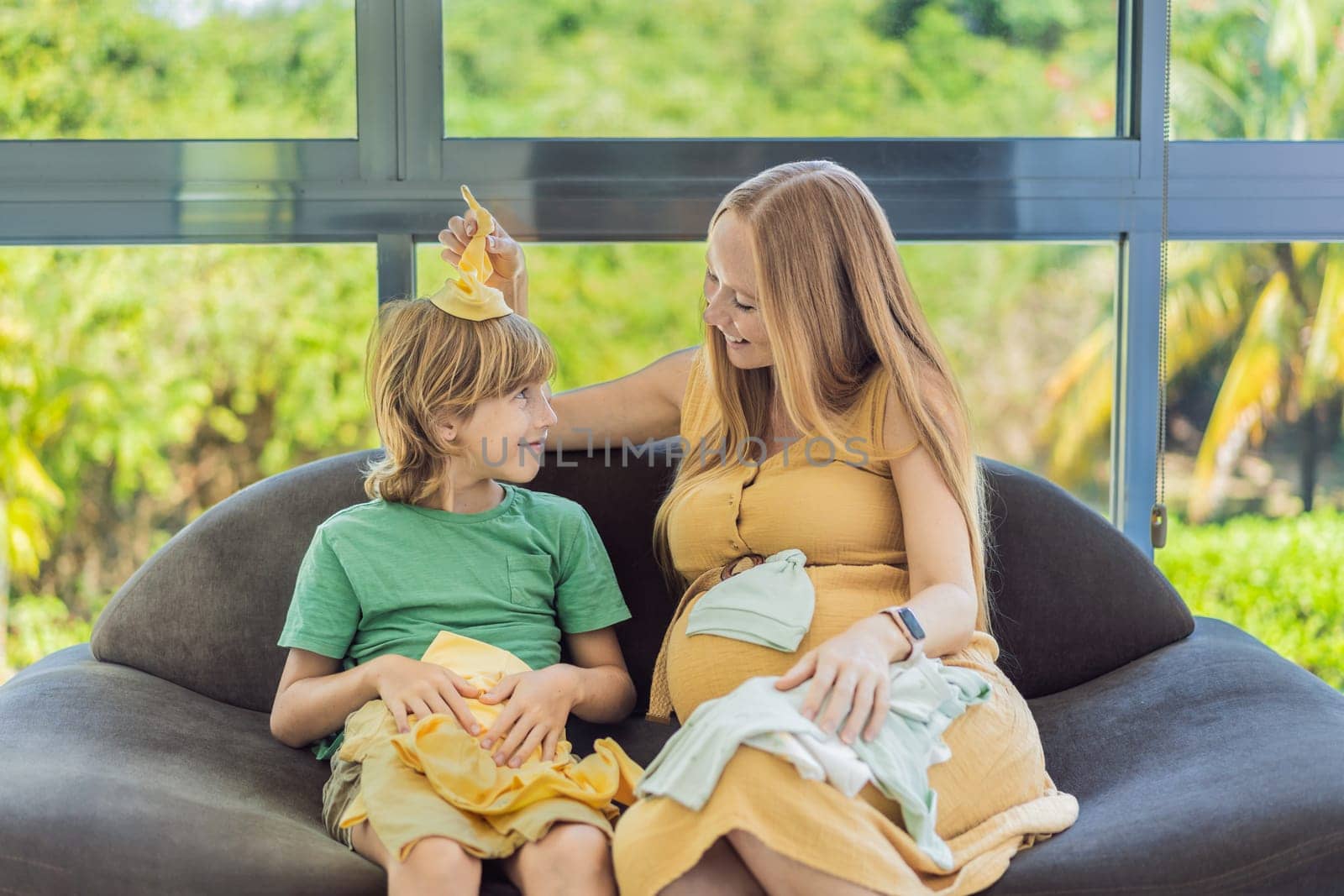 Heartwarming family moment as expectant mom and son joyfully browse through newborn baby's clothes, eagerly anticipating the arrival of a new family member by galitskaya