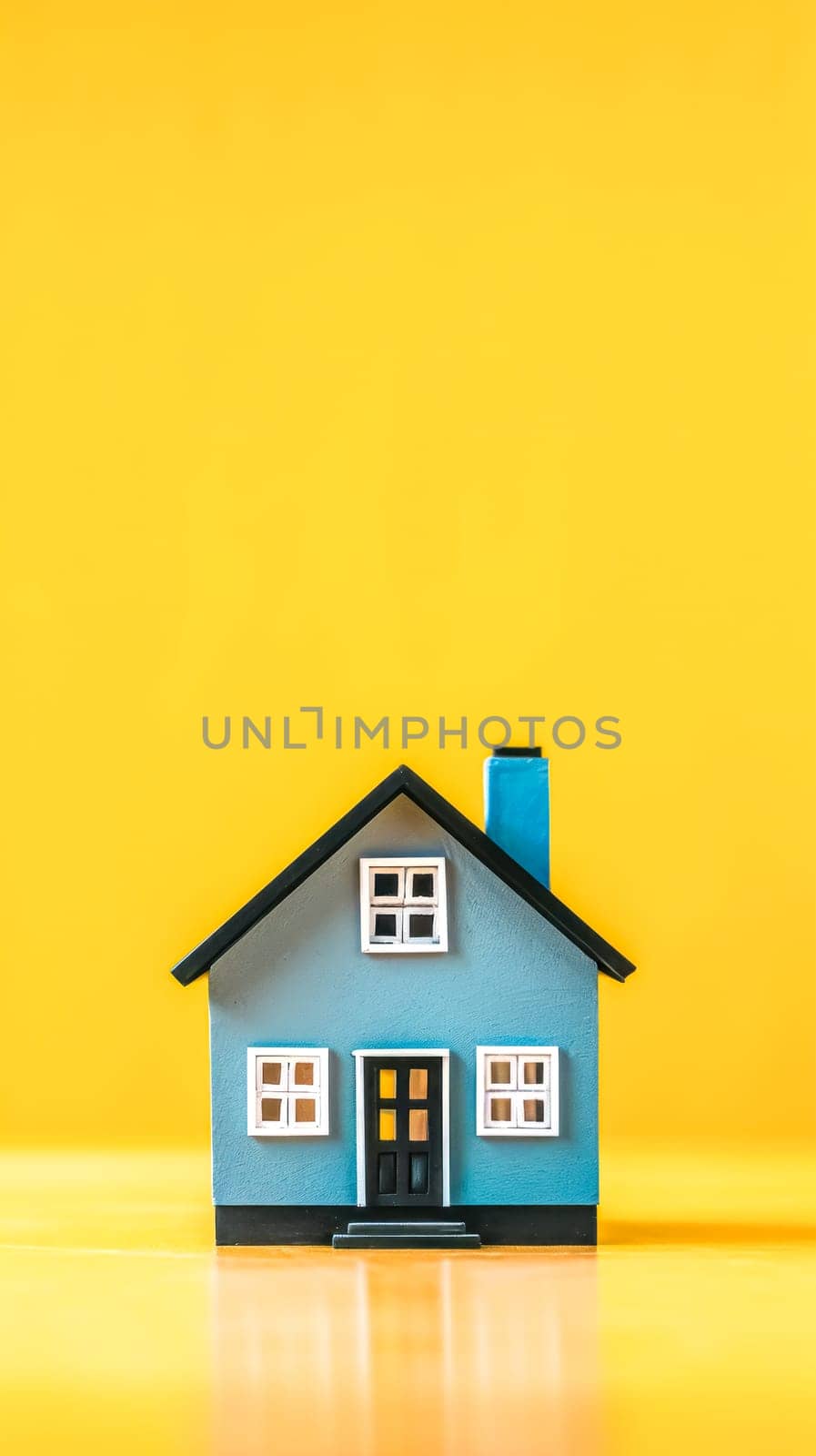miniature house with a blue facade and a bright blue chimney, set against a vibrant yellow background, evoking themes of home, comfort, and the simplicity of domestic life, vertical