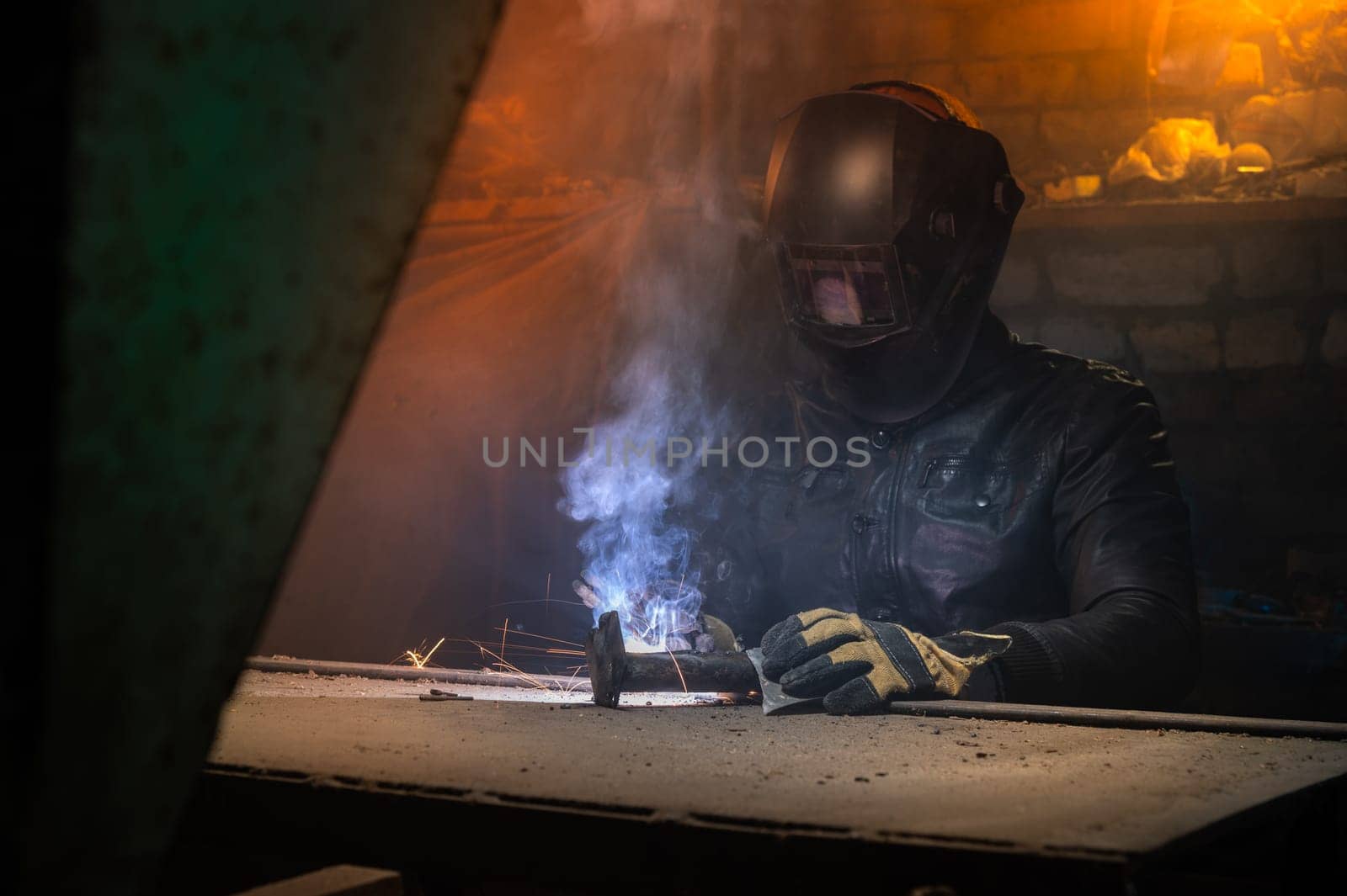 Village workshop, welding in an old garage. An unrecognizable man repairs a metal part wearing protective gloves and a mask.