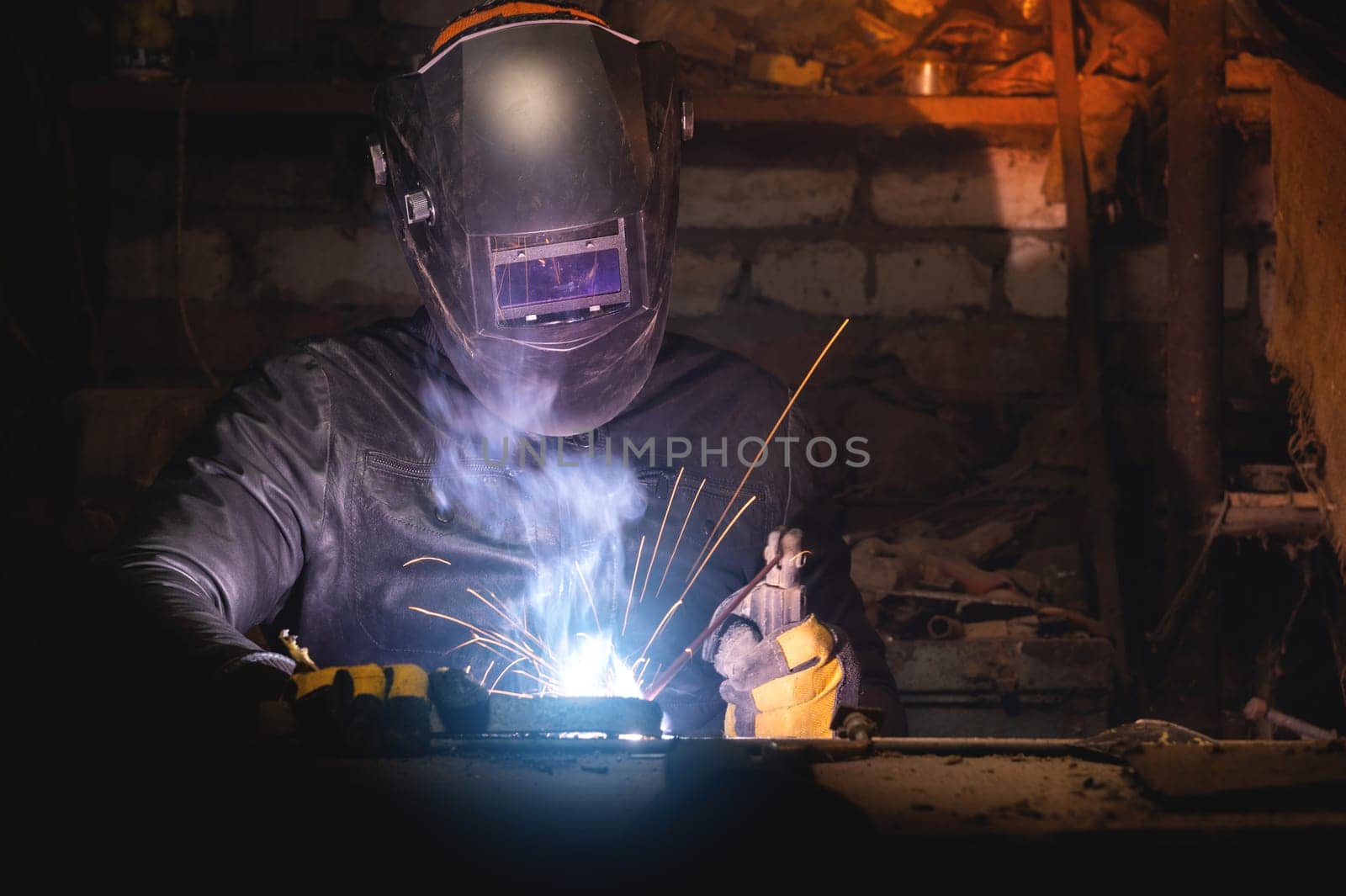 Village workshop, welding in an old garage. An unrecognizable man repairs a metal part wearing protective gloves and a mask by yanik88