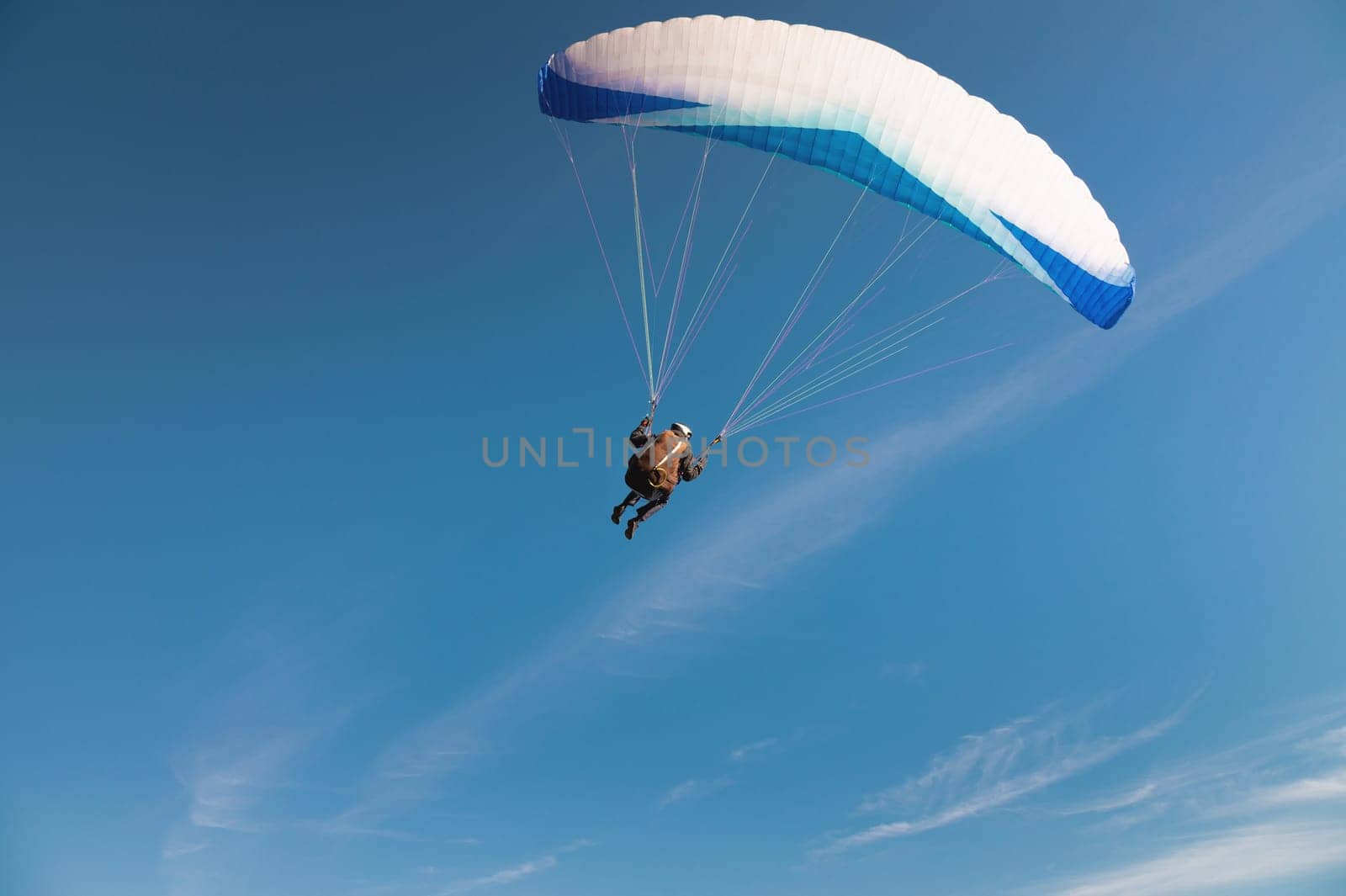 A paraglider takes off from a mountainside with a blue and white canopy and the sun behind. A paraglider is a silhouette. The glider is sharp, with little wing movement. A male paraglider launches a paraglider into the air.