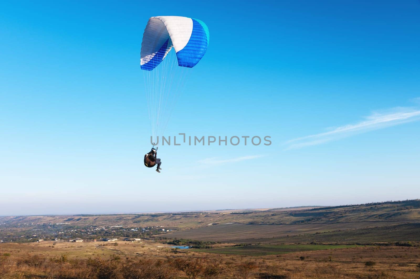 A paraglider takes off from a mountainside with a blue and white canopy and the sun behind. A paraglider is a silhouette. The glider is sharp, with little wing movement. by yanik88
