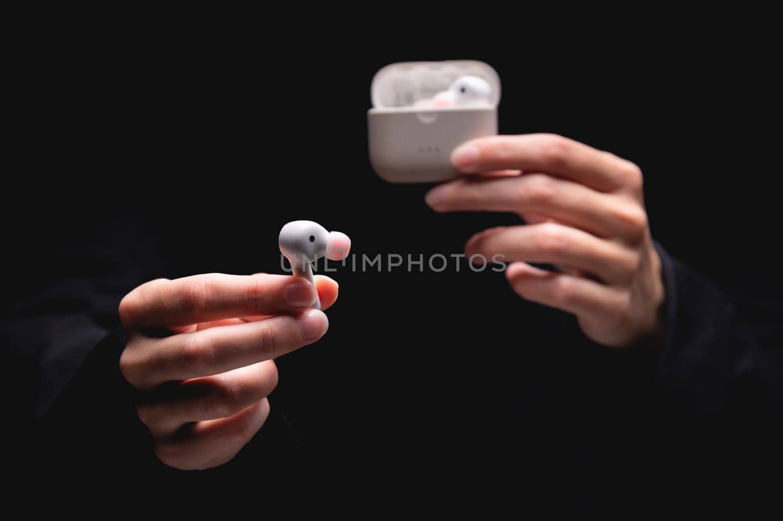 close-up of a woman taking a white wireless earphone out of the charger. Female hands touch the headphones of a portable gadget and present it forward to the camera on a black background by yanik88