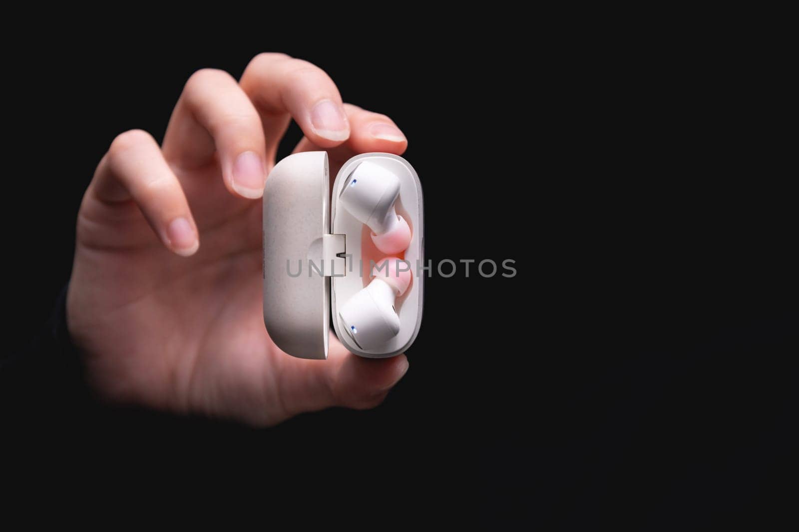 close-up of a woman taking a white wireless earphone out of the charger. Female hands touch the headphones of a portable gadget and present it forward to the camera on a black background.