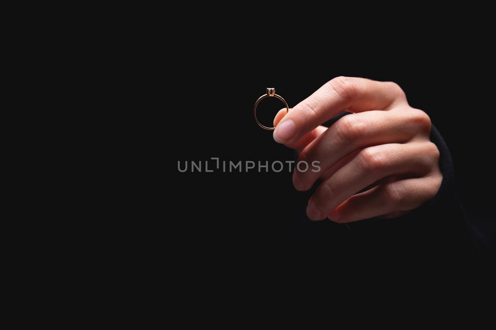 Diamond ring in a girls hand on a black background. Concept of love and wedding or divorce and unsuccessful marriage by yanik88