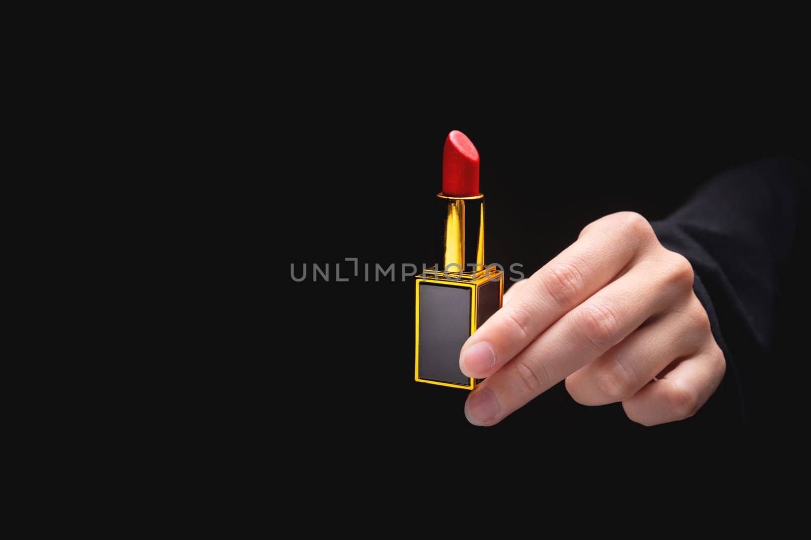 Red lipstick in a woman's hand on a dark background. Girl holding a popular cosmetic product.