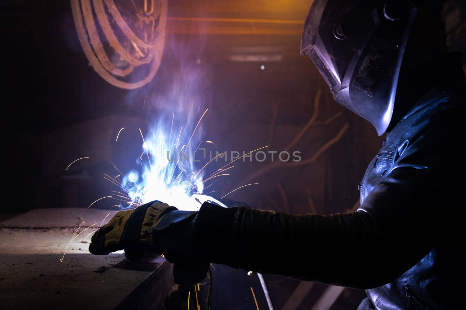 a man working with an electric welding machine. a man in safety glasses and a leather jacket cooks spare parts in his garage.