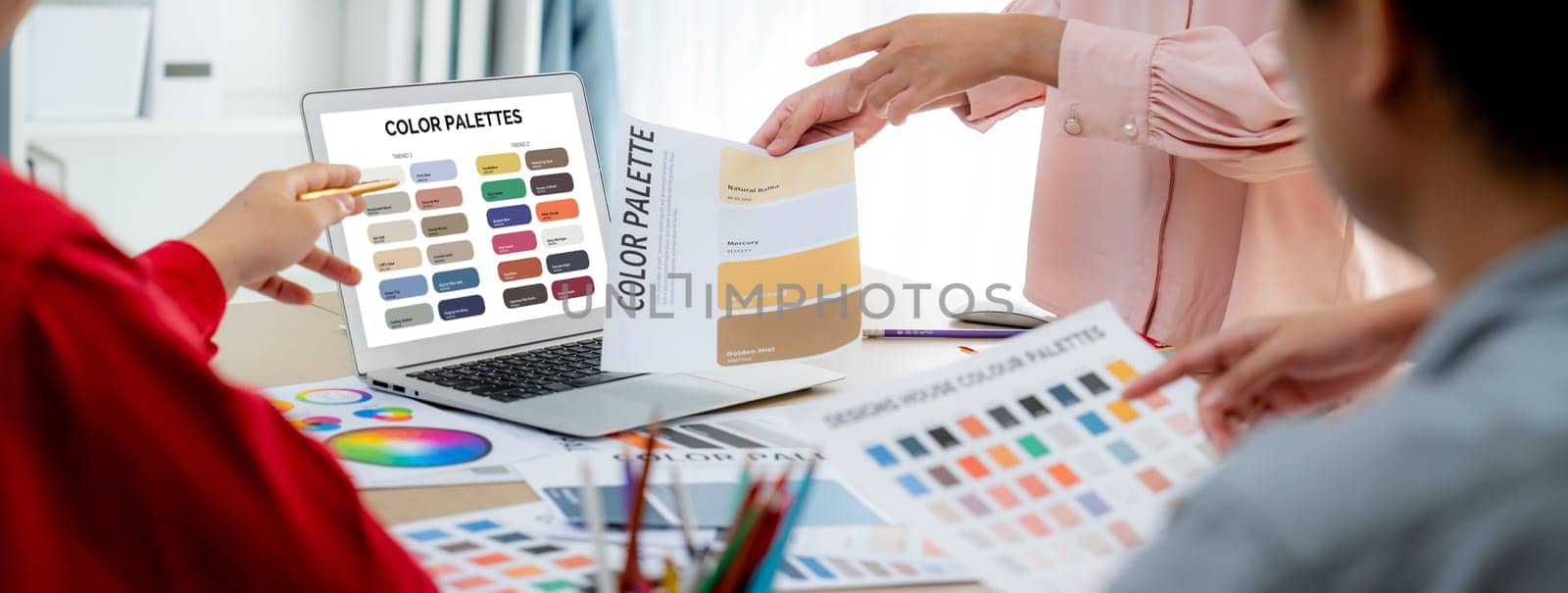 A portrait of creativity graphic designer team select appropriate color for the project by using laptop on table with equipment and designing tool scatter around at modern office. Closeup. Variegated.