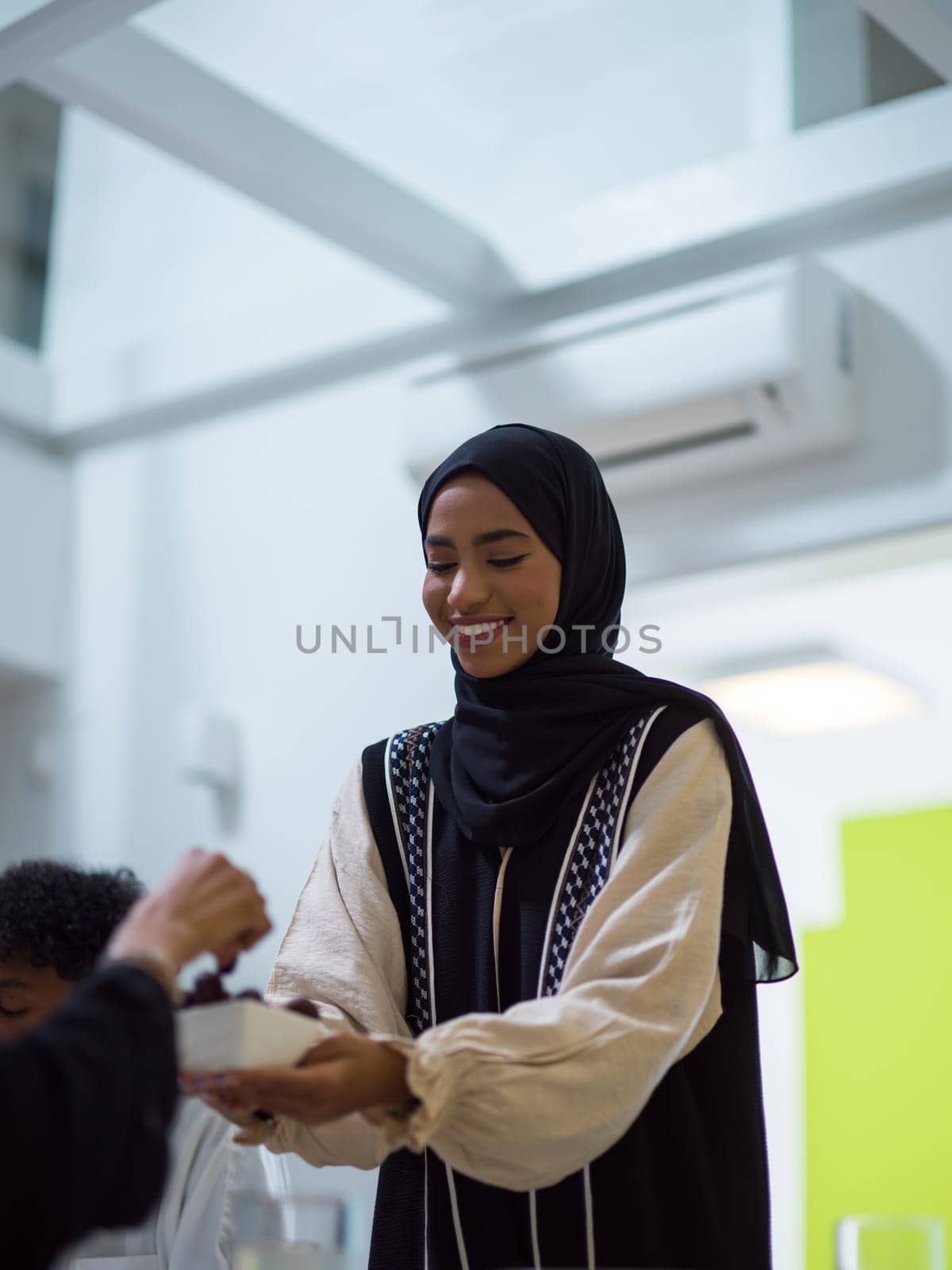 A woman in a hijab extends a platter of dates to her diverse family, creating a scene of unity and joy as they come together to break their fast during the holy month of Ramadan, symbolizing the shared love and spiritual connection within their cultural and religious traditions.