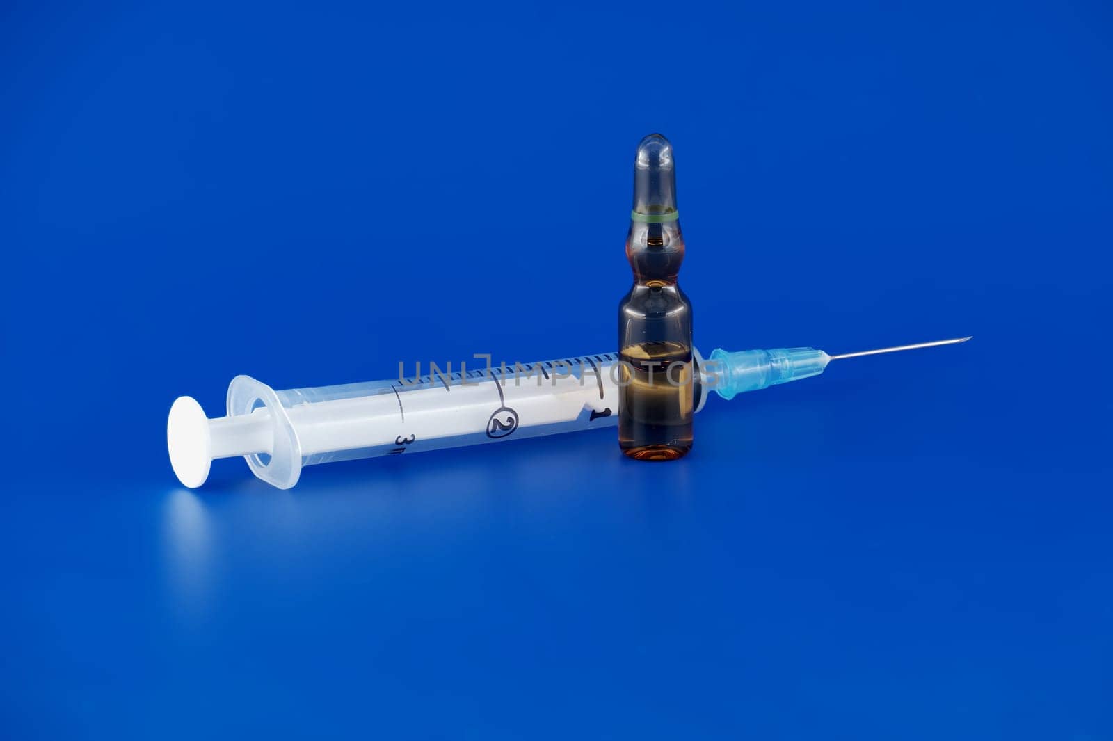 Close-up view of syringe and ampoule against a blue background, quintessential medical tools for medical treatment and vaccination