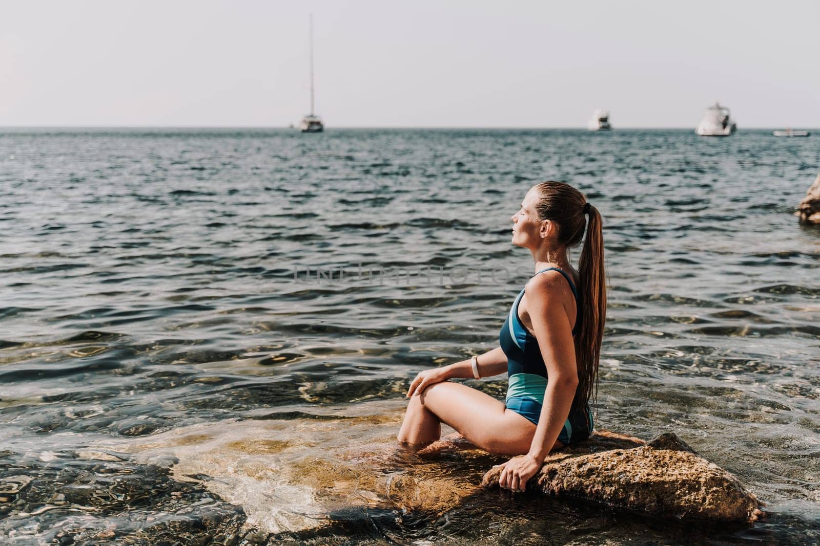 Woman beach vacation photo. A happy tourist in a blue bikini enjoying the scenic view of the sea and volcanic mountains while taking pictures to capture the memories of her travel adventure