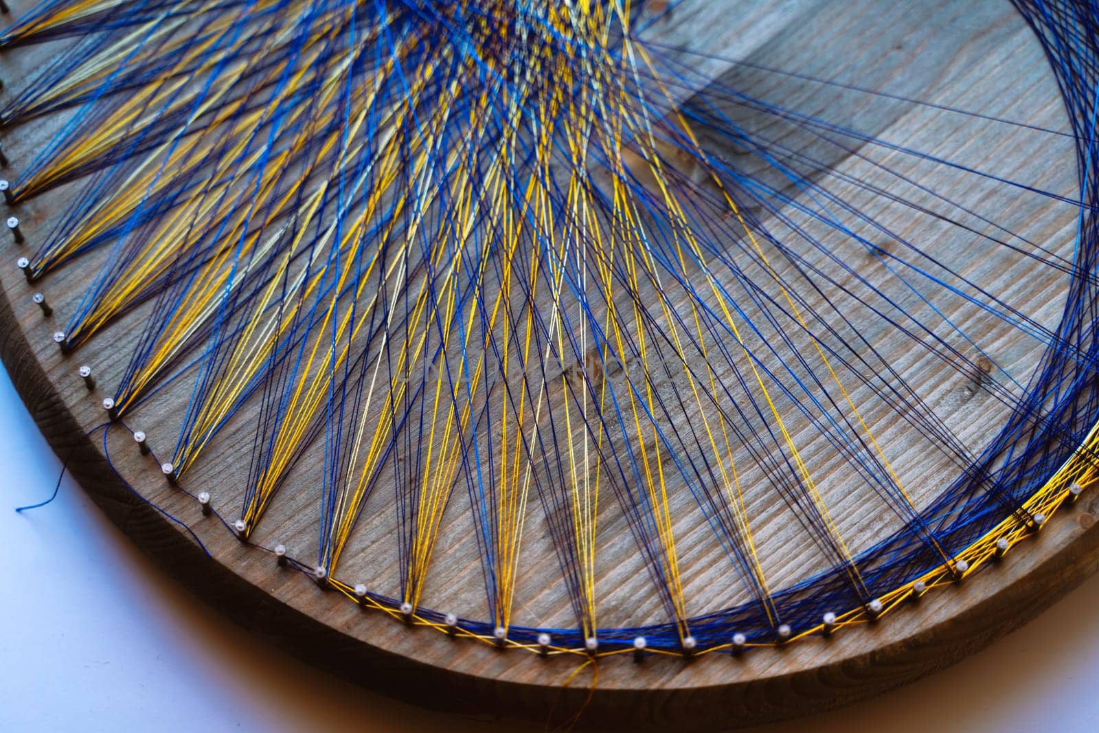 Colored thread mandala on a wooden board with nails. Mandala Moon Harmony Sun esotericism and psychology pictures from yellow and blue silk threads