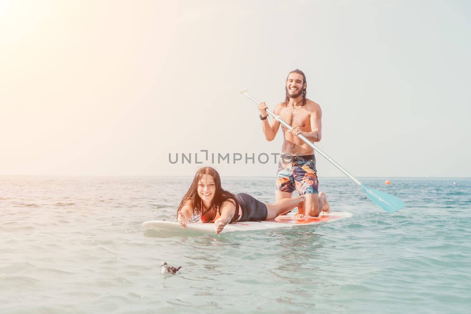 Sea woman and man on sup. Silhouette of happy young woman and man, surfing on SUP board, confident paddling through water surface. Idyllic sunset. Active lifestyle at sea or river