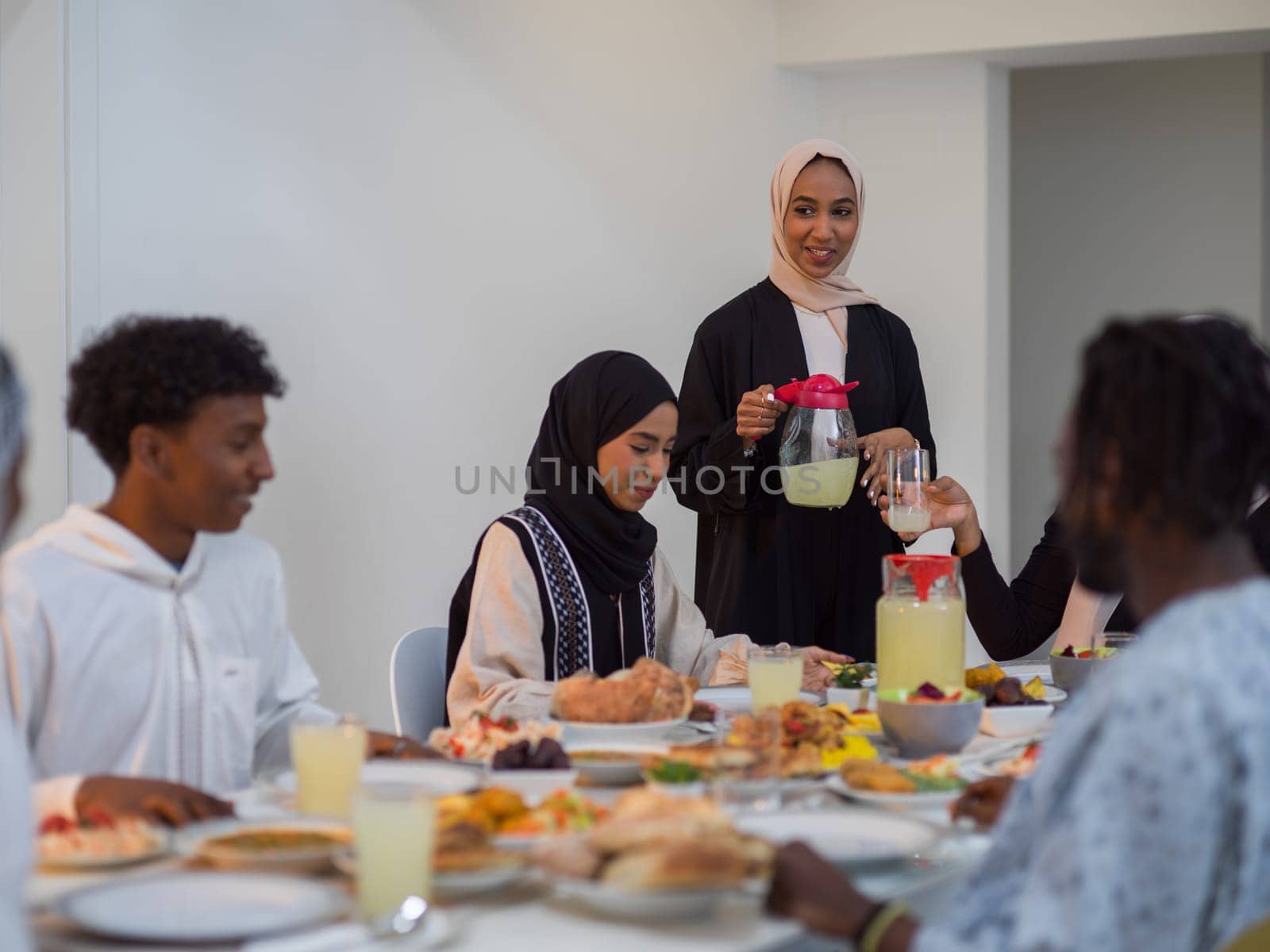 A diverse Islamic family gathers for iftar, joyfully breaking their fast together during Ramadan, with a Muslim woman in a beautiful hijab gracefully pouring water to mark the end of their fast, showcasing the unity, love, and spiritual connection that define this special family moment by dotshock