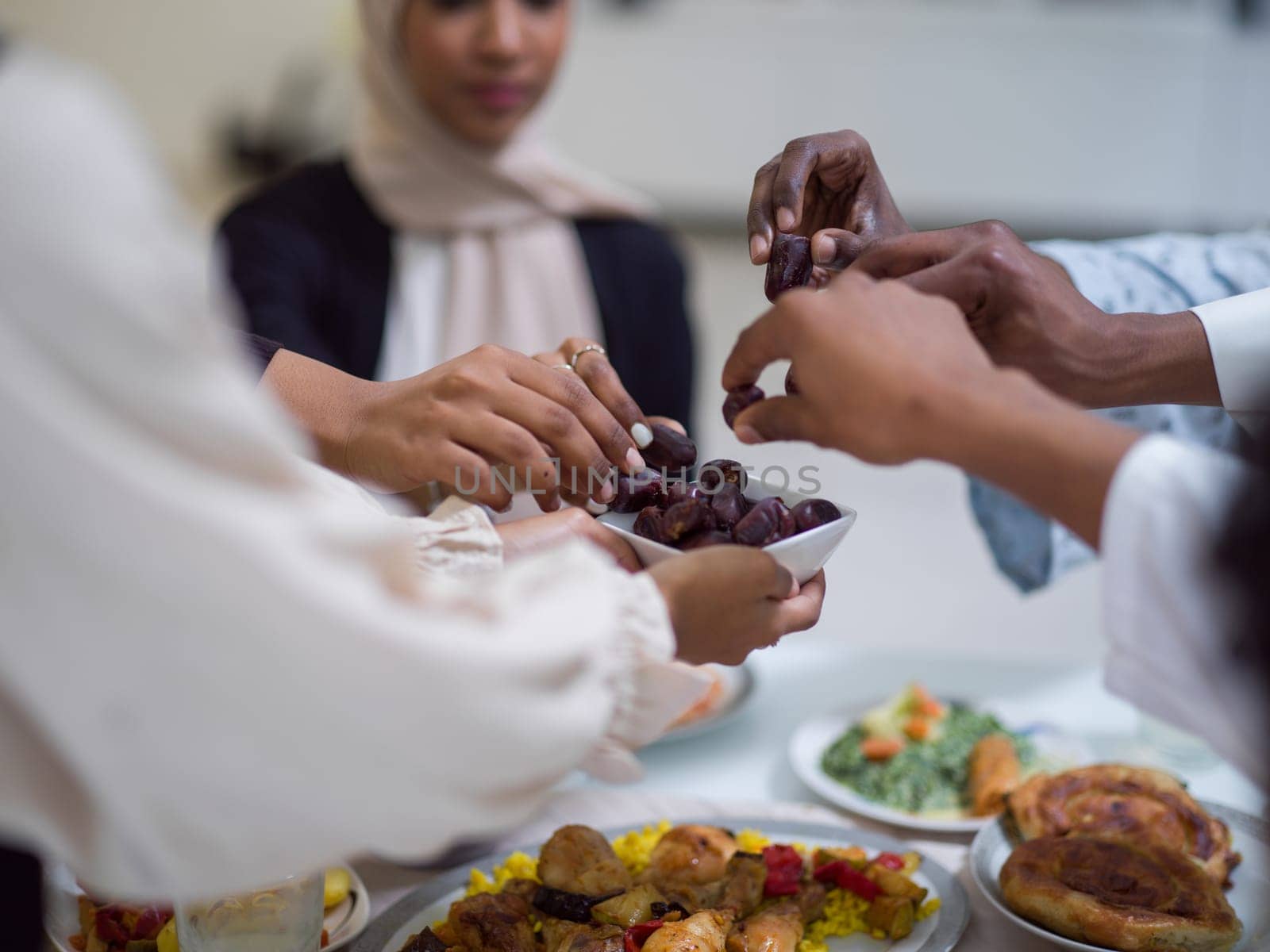 A woman in a hijab extends a platter of dates to her diverse family, creating a scene of unity and joy as they come together to break their fast during the holy month of Ramadan, symbolizing the shared love and spiritual connection within their cultural and religious traditions by dotshock