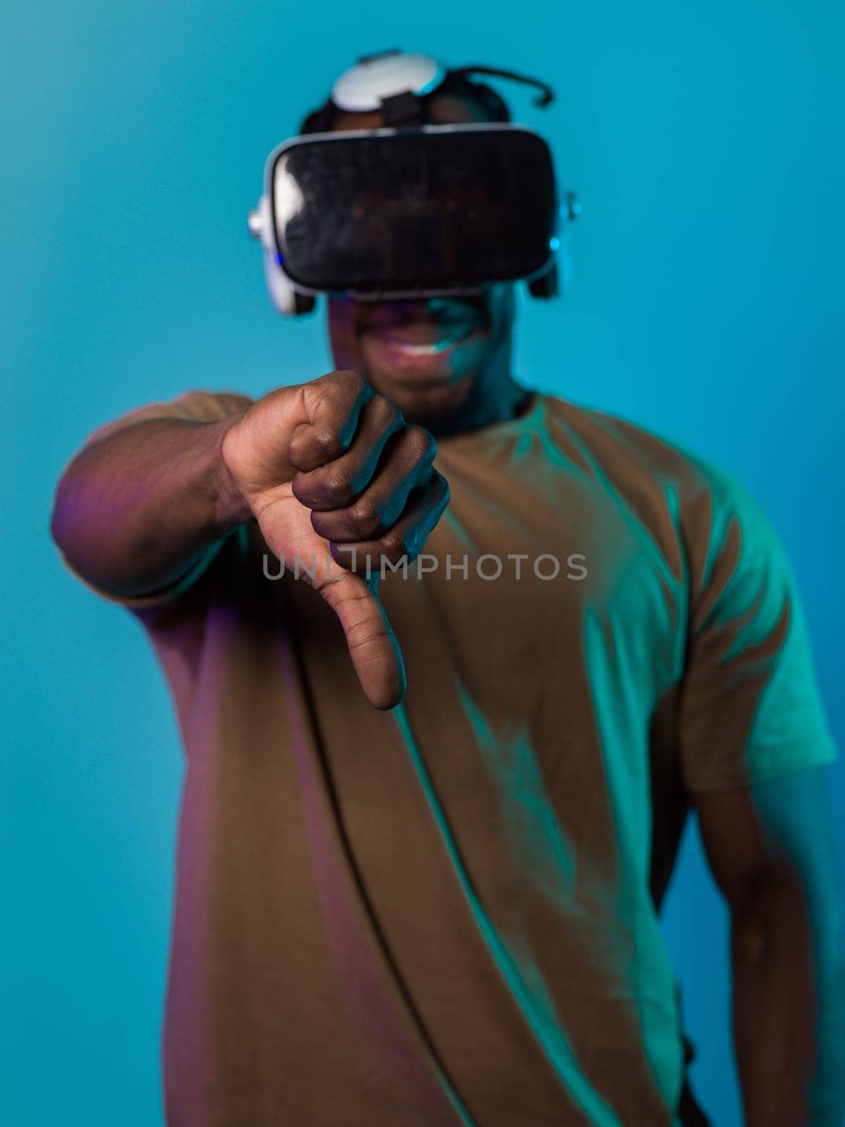 African American man, wearing virtual reality glasses, expresses dissatisfaction by pointing down with his hand while standing isolated against a blue background, portraying a modern critique within the immersive digital realm.